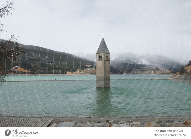 Der versunkene Kirchturm der Pfarrkirche von Alt-Graun im sehr leeren Reschensee in Südtirol und zwei Spaziergänger mit Hund auf der Sandbank Stausee Turm