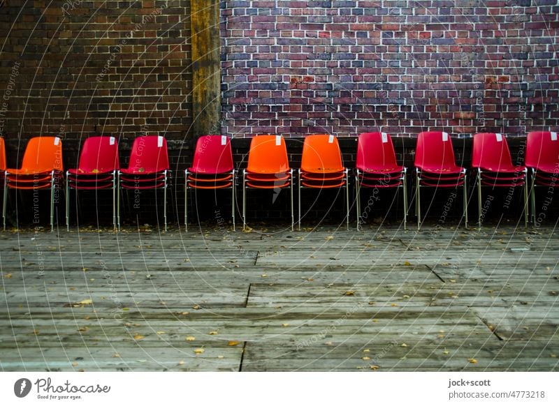 Alle Stühle zur Seite gestellt Reihe Sitzgelegenheit Bestuhlung Platz Menschenleer Stuhlreihe Sitzreihe Backsteinwand Podest Holzbrett Plastikstuhl viele