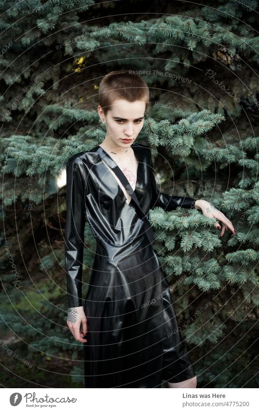 Ein kurzes Haar hübsches Mädchen in schwarzem Latex mit einem grünen Wald Hintergrund. Steht hier und zeigt ihre Schönheit, Tattoos und Stil. Giving einige launische Vibes mit mehr Fragen als Antworten beantwortet werden.