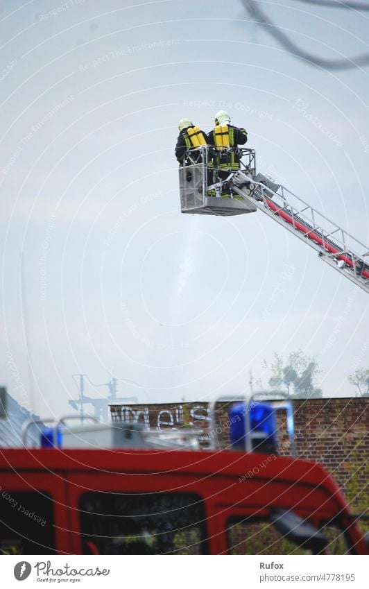 Die Feuerwehr ist mit Einsatzfahrzeugen und einem Kran im Einsatz. Sie löscht das Feuer von oben aus. Feuerwehrmann Feuerwehrleute Feuerwehreinsatz