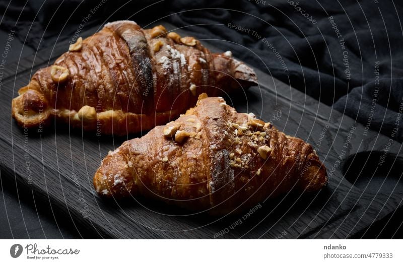 Gebackene Croissants auf einem schwarzen Holzbrett, bestreut mit Puderzucker, Ansicht von oben Frühstück Lebensmittel Bäckerei Gebäck Brot braun gebacken frisch