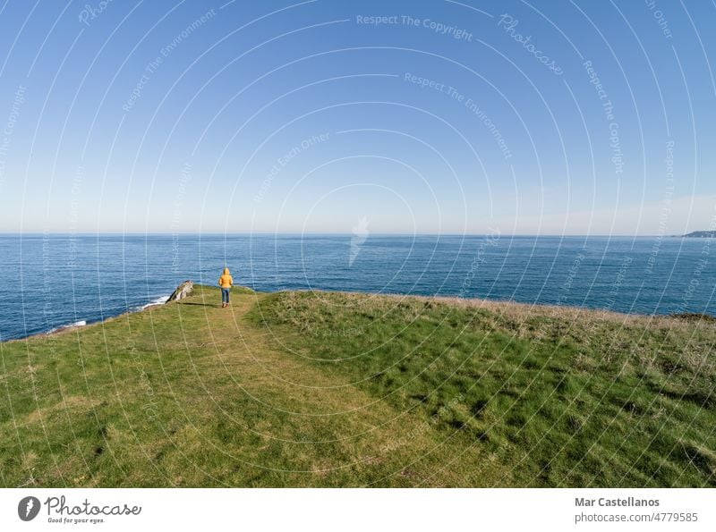 Küstenlandschaft und Mädchen in gelbem Kapuzenmantel, das aufs Meer schaut und spazieren geht. Raum kopieren. Landschaft MEER Himmel Küstenlinie Frau Person