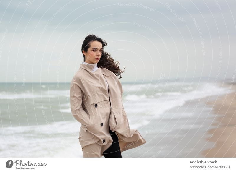 Frau steht am Meeresufer in der Nähe des wogenden Meeres Küste Strand Wasser MEER Wind Seeküste winken Küstenstreifen feminin fliegendes Haar Wetter Ufer Dame