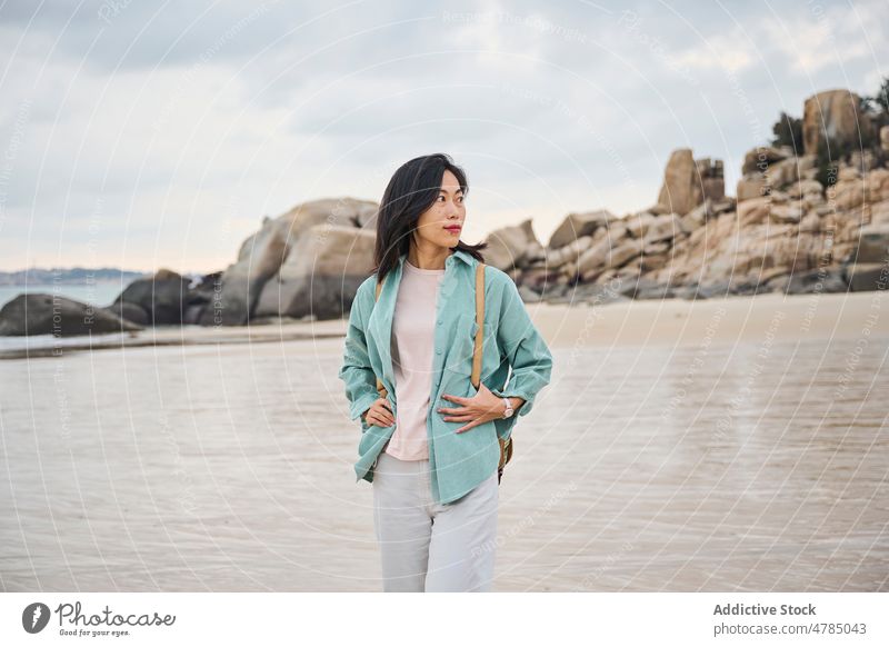 Schönes asiatisches Mädchen, das während ihrer Reise im Herbst am Strand spazieren geht Natur Steine laufen wolkig Sand Spaziergang nass nasser Sand