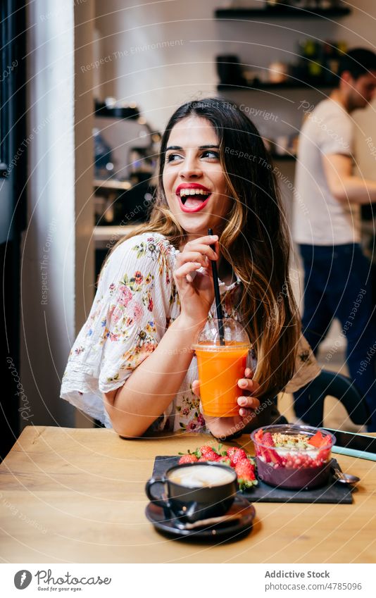 Glückliche junge Frau frühstückt und trinkt Saft in einem Cafe genießen Tasse Frucht Café trinken freudig Smoothie Schüssel Vegetarier Beeren Veganer frisch