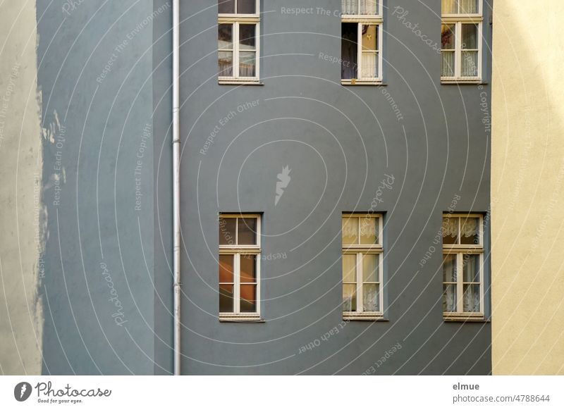 Blick auf ein im Schatten liegendes, grau-blaues Mehrfamilienhaus / wohnen Fenster Mietshaus Fallrohr Wohngebiet Stadtwohnung Mietpreisbremse Mietpreise