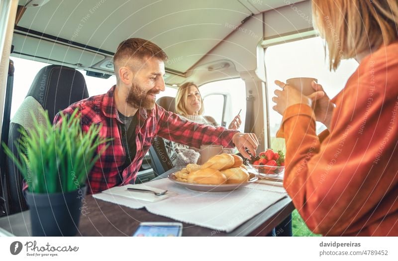 Freunde beim morgendlichen Frühstück im Wohnmobil Wohnwagen Kleintransporter genießen entspannend Lächeln Morgen Brötchen Frucht Blaubeeren Erdbeeren