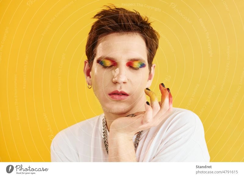 Junger schwuler Mann steht im Studio und posiert für eine Kamera. Regenbogen Make-up jung Porträt Gesicht Geschlecht lgbt Typ Transgender androgyn gelb