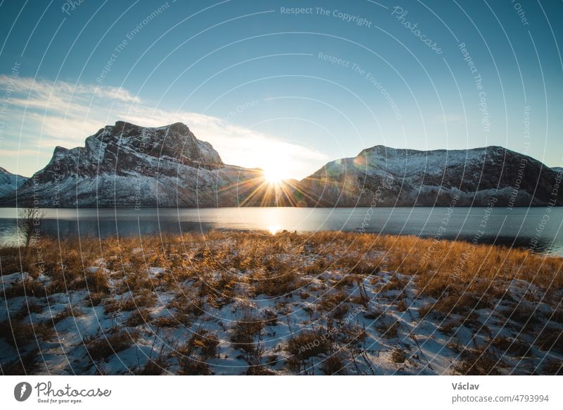 Der Sonnenaufgang erhebt sich hinter zwei verschneiten Felsen. Die Landschaft im Dorf Bergsbotn auf der Halbinsel Senja in Nordnorwegen, Skandinavien, befindet sich im Winterschlaf.