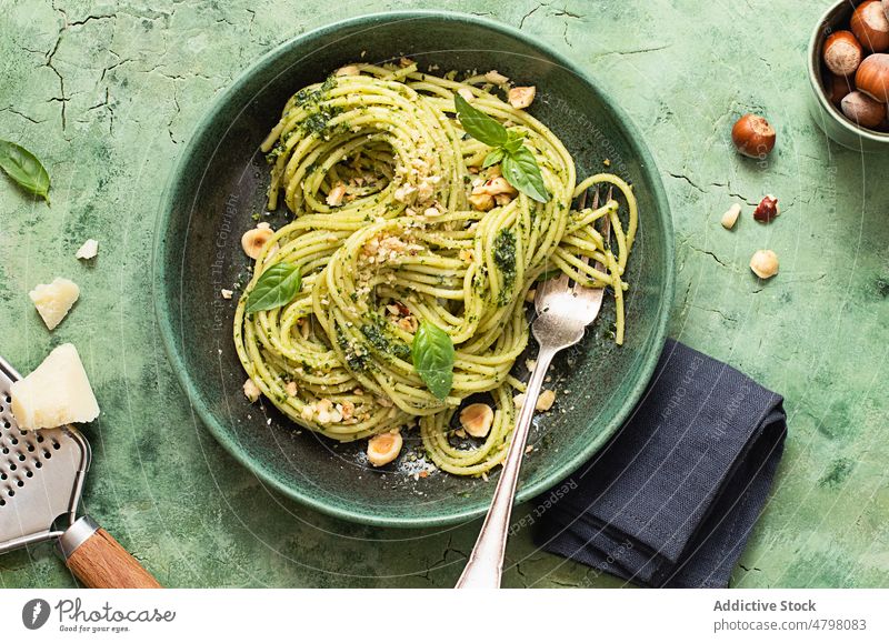 Keramikteller mit Haselnuss-Pesto-Spaghetti auf grüner Tischoberfläche Schalen & Schüsseln rustikal Abendessen kulinarisch Basilikumblätter Serviette