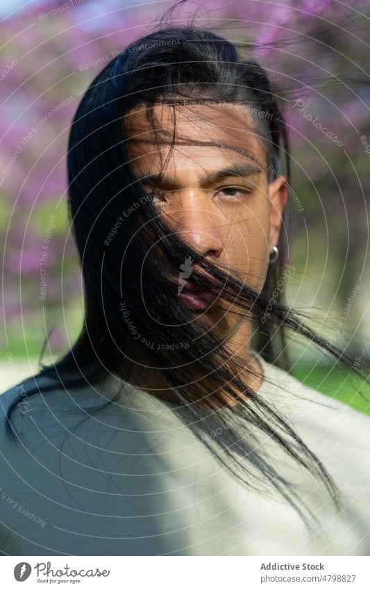 Hispanischer Mann im Park stehend Vorschein Stil trendy Straße Baum Schatten Sommer Sonnenschein gutaussehend lange Haare hispanisch männlich Windstille jung