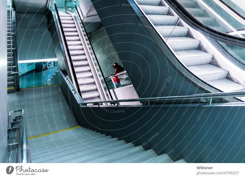 Ein System aus Treppen und Rolltreppen führt in die Tiefe, eine junge Frau in roter Jacke dreht sich um Untergrund runter hoch abwärts aufwärts unterirdisch