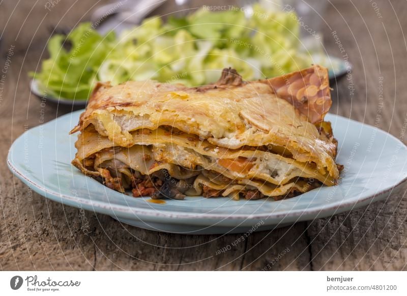 Lasagne mit Salat auf dunklem Holz Messer Gabel Wein Mahlzeit Essen Italienisch Küche Pasta rustikal Teller Portion Käse Rindfleisch mediterran Mozzarella