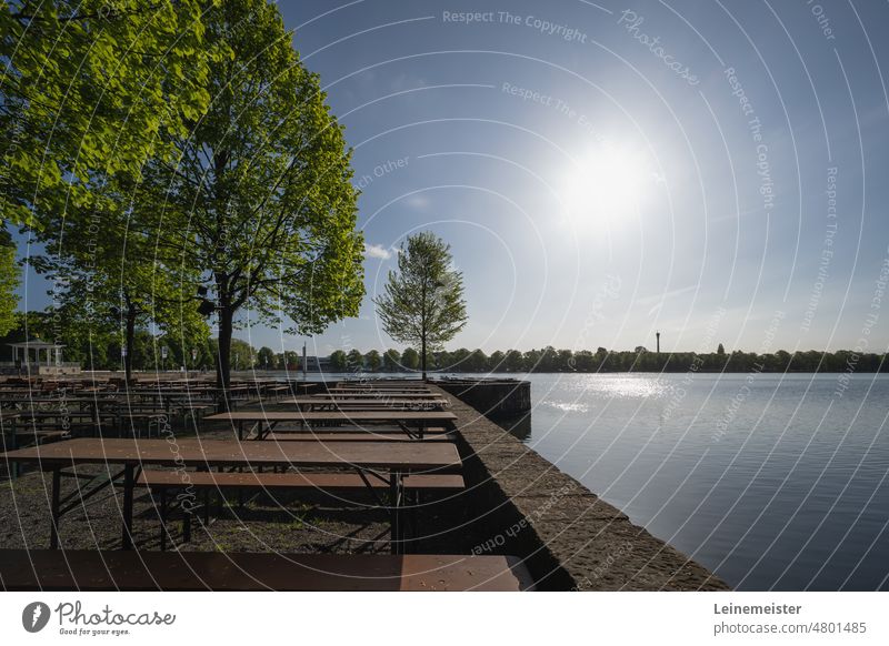 In einem Biergarten an einem frühen Sonntagmorgen im Mai am Maschsee in Hannover Frühling Sonne Bäume See leer Bänke Tische Skyline ufer Morgen Mauer