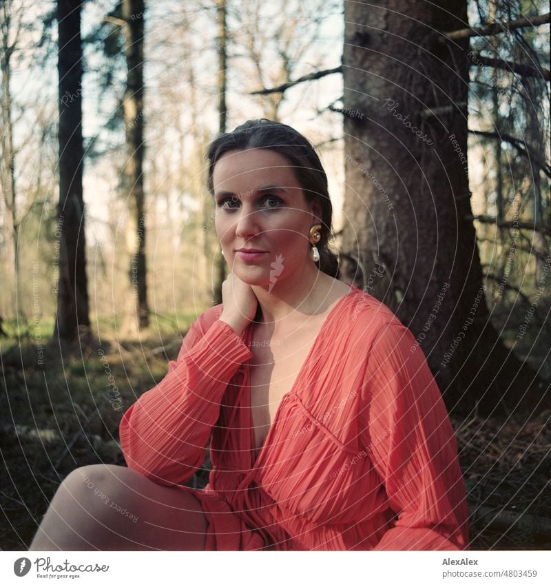 analoges Mittelformat-Portrait einer jungen Frau in orangem Kleid, die in einem Wald sitzt junge Frau schön feminin weiblich Identität authentisch ästhetisch