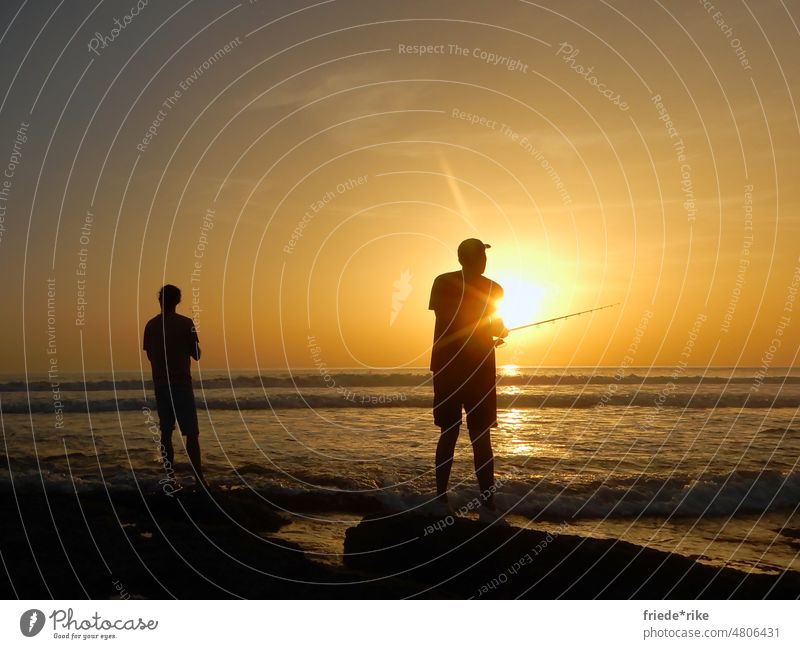 Angler am Meer bei Sonnenuntergang Mann Strand Spanien Andalusien Wolken Felsen Wasser Silhouette orange Atlantik Costa de la Luz blaue Stunde Sonnenlicht Küste