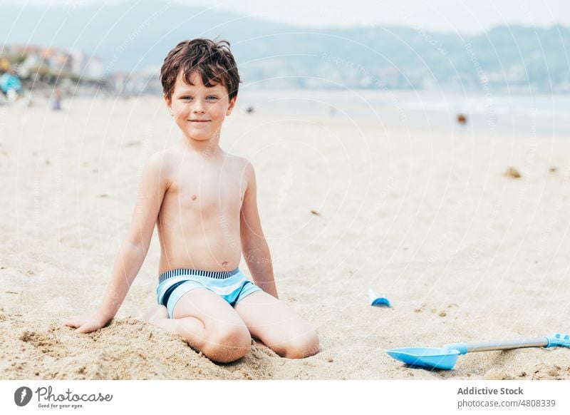 Fröhlicher kleiner Junge gräbt Sand am Strand Graben Sommer Urlaub Lächeln schaufeln Wochenende froh Kind Küste sich[Akk] entspannen Ufer knien Kindheit ruhen