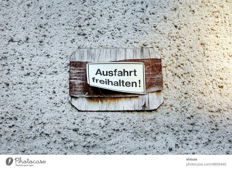 kleines Schild  - Ausfahrt freihalten ! -   auf einer größeren, langsam zerfallenden Holzplatte an einer grob verputzten Wand Aufforderung Mitteilung Spanplatte