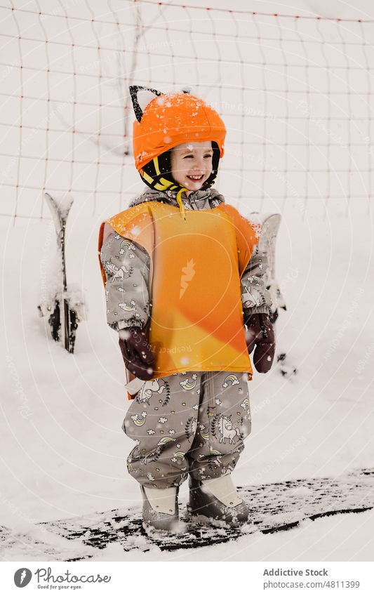 Fröhliches Kind in Winteroverall und Helm lächelnd in verschneitem Terrain Lächeln Schnee Skifahrer Skigebiet Aktivität heiter gesamt Kindheit Feiertag Hobby