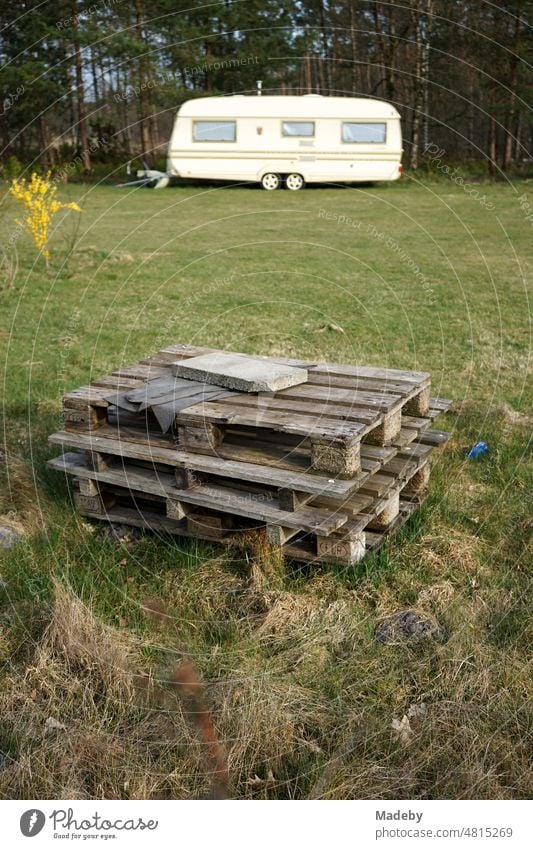 Gestapelte Europaletten aus Holz auf grünem Rasen im Frühling mit Wohnwagen für Camping und Vanlife auf dem Campingplatz am Segelflugplatz Oerlinghausen bei Bielefeld im Teutoburger Wald in Ostwestfalen-Lippe