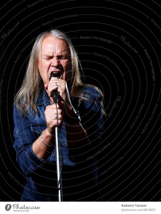 älterer Mann mit langen grauen Haaren singt in ein Mikrofon lange Haare singen Gesang Schauplatz schwarz Hintergrund Musik alt Senior männlich Sänger Glück