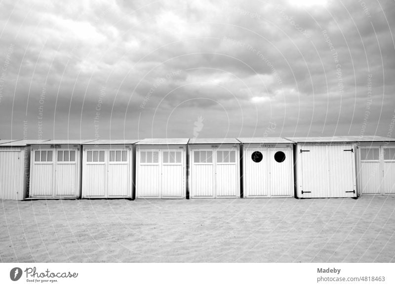 Traditionelle weiße Strandkabinen mit Wolkenhimmel am Strand in Knokke-Heist an der Nordsee bei Brügge in Westflandern in Belgien, fotografiert in klassischem Schwarzweiß