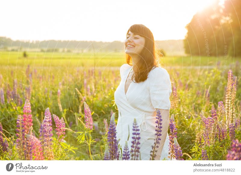 Schöne Frau im weißen Sommerkleid genießt die sommerliche Natur. Pflücken bunte Blumen, atmen frische Luft und Blumenduft, zu Fuß in der sonnigen Feld von Lupinen. Glück Konzept