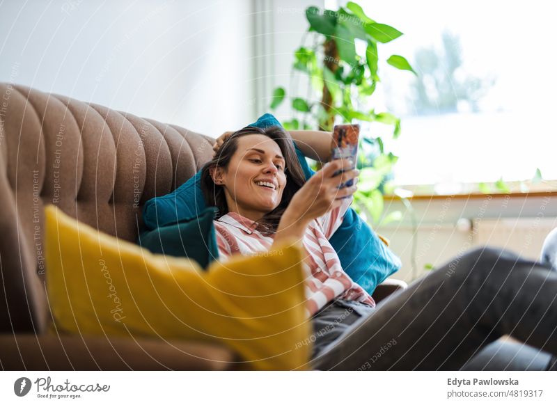 Glückliche junge Frau, die auf dem Sofa ein Mobiltelefon benutzt Handy Smartphone Technik & Technologie online Internet per Telefon Mitteilung häusliches Leben