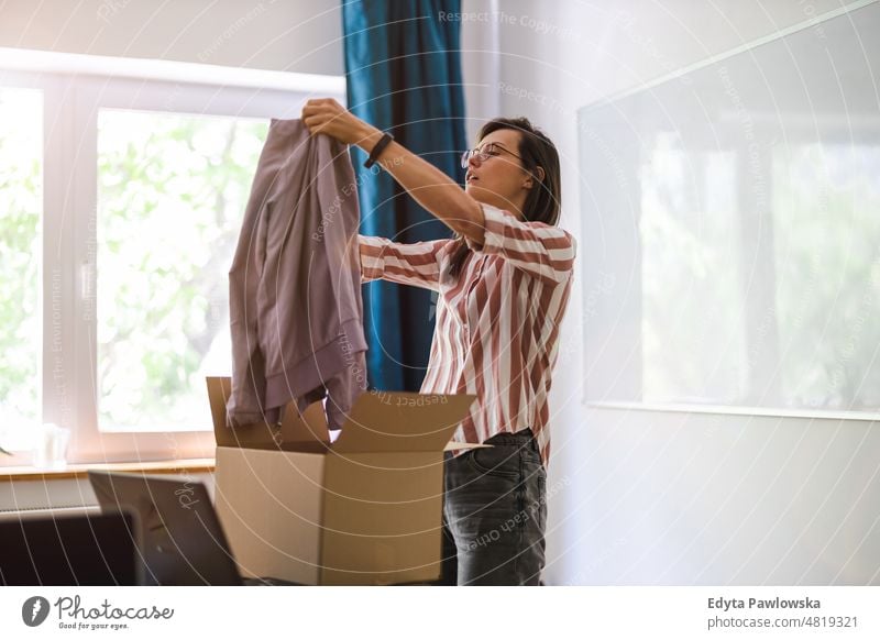 Frau beim Auspacken eines gekauften Pakets mit Kleidung häusliches Leben Selbstvertrauen im Innenbereich heimwärts Haus Menschen jung Erwachsener lässig