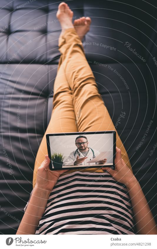 Frau liegt auf einem Sofa und spricht mit einem Arzt online über ein digitales Tablet. Telemedizinisches Konzept. Technik & Technologie Medizin geduldig