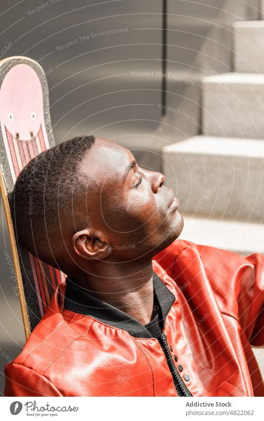 Ruhiger afroamerikanischer Mann lehnt sich auf Skateboard auf Straßentreppe Augen geschlossen sich[Akk] entspannen Treppenhaus trendy cool Skater Freizeit ruhen