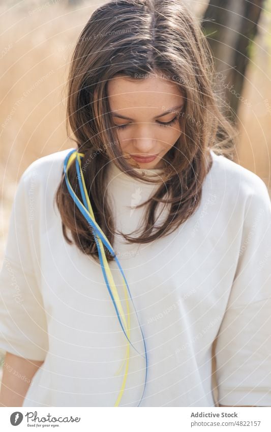 Dame mit blauen und gelben Bändern im Haar in der Natur stehend Frau Ukrainer Fahne Bändchen Lächeln Windstille Patriotin Porträt feminin Feld Sonnenlicht