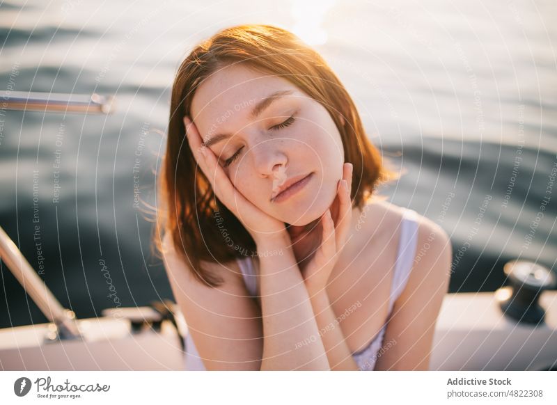 Friedliche Dame, die ihr Gesicht berührt, während sie sich auf einem Segelboot mit geschlossenen Augen entspannt Frau Kreuzfahrt MEER Augen geschlossen