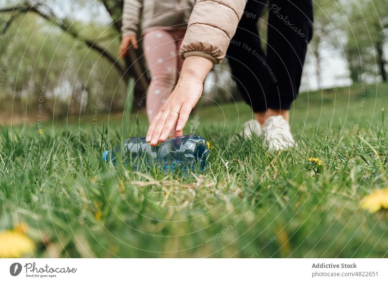 Gesichtslose Frau mit Kind, die eine Flasche von einer Wiese aufhebt abholen Ökologie Natur Wald Mutter Tochter Müll Park Zeit verbringen Ökosystem behüten