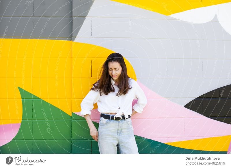 Junge Frau in weißem Hemd und hellblauen Jeans stehen in der Nähe von bunten lebendigen Wand. Candid Lifestyle Sommer Stil Porträt. schön Großstadt Glück