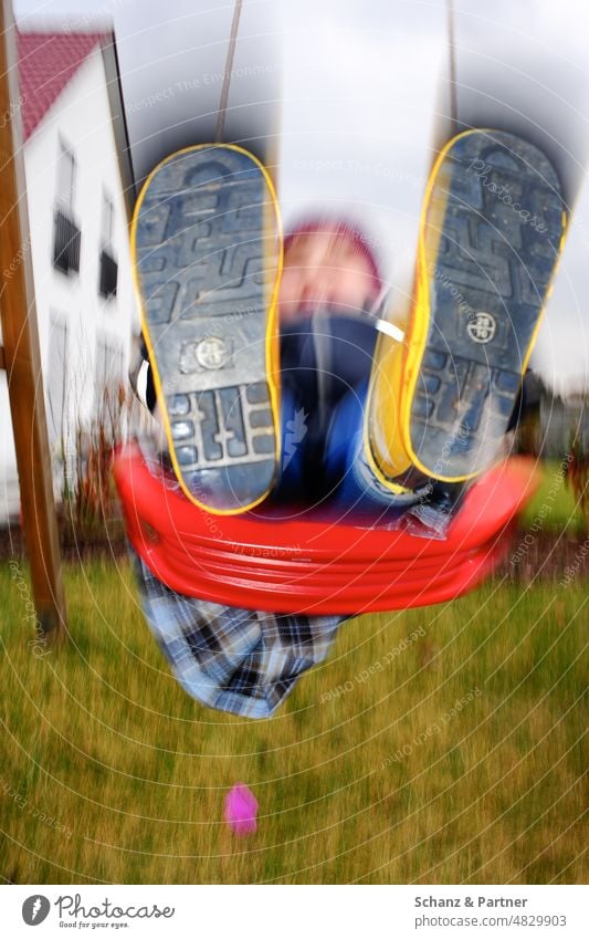 Kind mit Gummistiefeln schaukelt im Garten Bewegungsunschärfe Schaukel spielen Familie Eigenheim Familienleben verwischt Spaß Kindheit Spielen Freude schaukeln