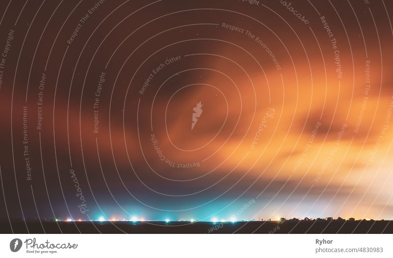 Night Sky With Rare Glowing Stars Shining Through The Cloudiness Overcast Above Countryside Town Landscape. Ländliches Feld Wiese im frühen Frühling sternenklar