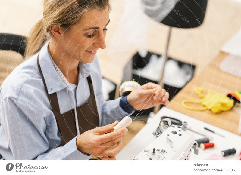 Junge Schneiderin näht Kleider am Arbeitstisch. Lächelnde Näherin und ihre Hand in Nahaufnahme in der Werkstatt. Fokus auf die Naht auf dem Tisch Maschine