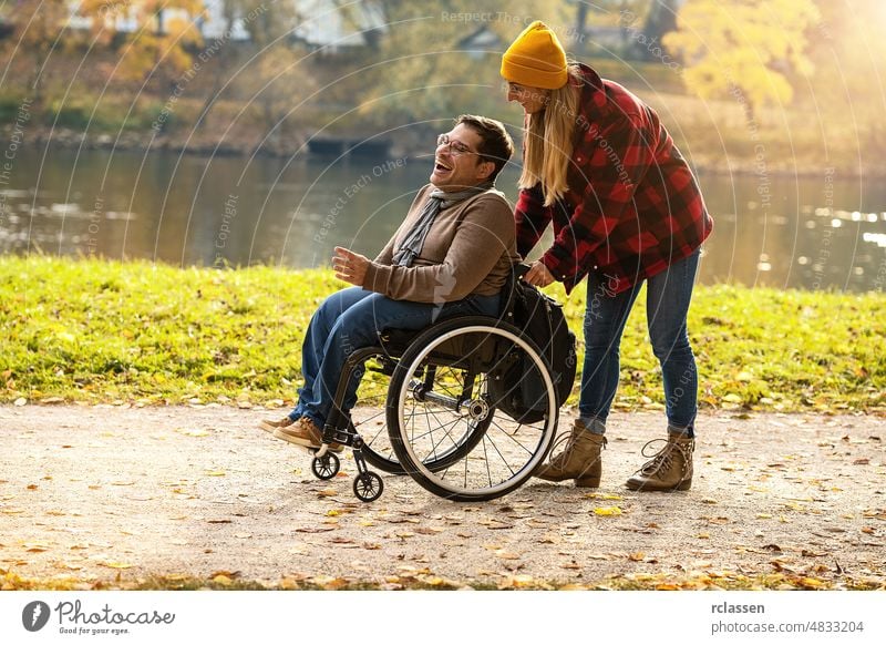 Frau und ihr Freund im Rollstuhl machen einen Spaziergang durch den Park an einem Fluss und genießen den Herbst Behinderung Großstadt Paar Freunde Deutschland