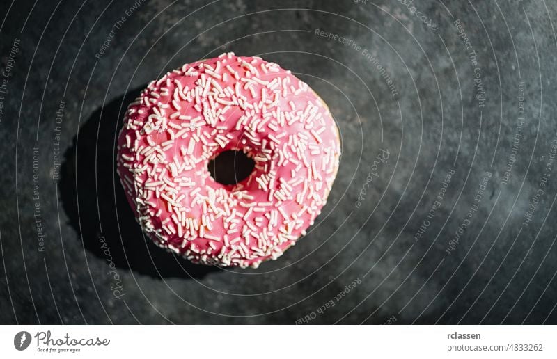 Donut mit rosa Glasur und Streuseln auf einem dunklen Tisch Krapfen sortiert gebacken Bäckerei Frühstück Kuchen Kalorien Schokolade Farbe farbenfroh lecker