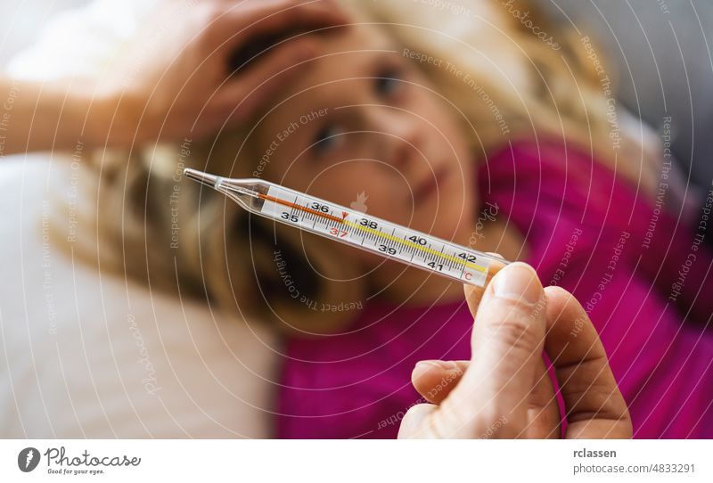 Thermometer in der Hand der Mutter, die die Temperatur ihres kranken Kindes misst. Krankes Kind mit hohem Fieber im Bett liegend und Mutter hält Thermometer. Hand auf der Stirn.