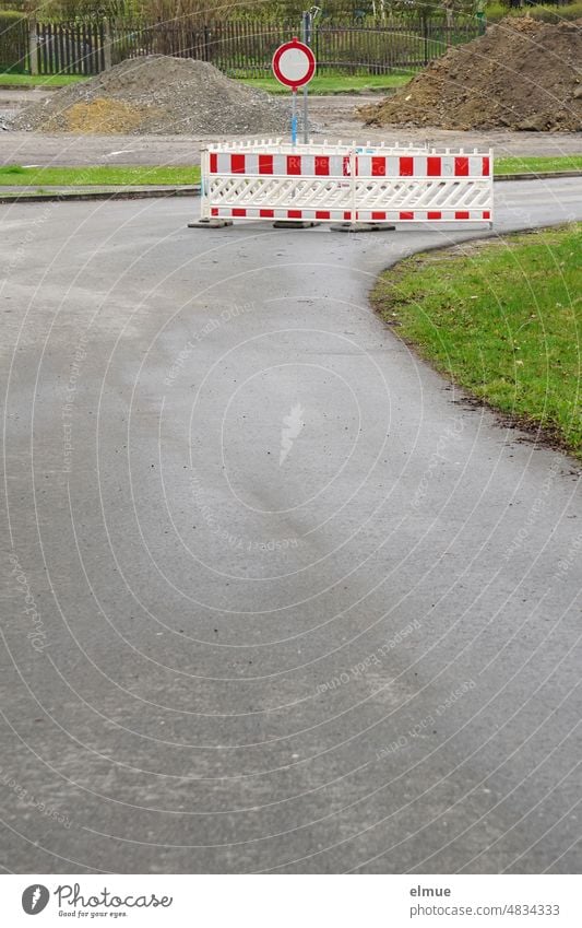 Absperrschranken und ein Verkehrszeichen - Verbot für Fahrzeuge aller Art - stehen auf einer abbiegenden grauen Asphaltstraße vor Erd- und Splitthaufen / Baustelle / Straßensperrung