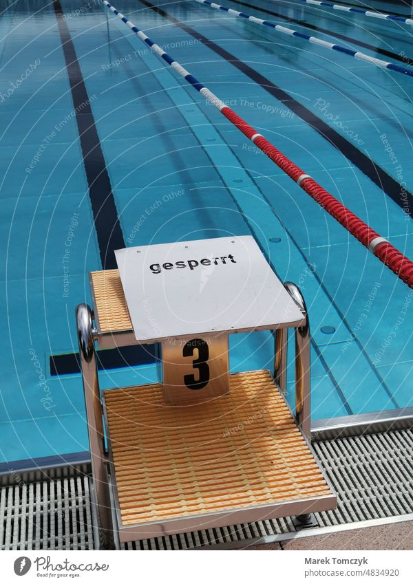 Gesperrter Startblock im menschenleeren Schwimmbad. Klares Wasser ohne Wellen. Freibad gesperrt Schwimmsport Sommerzeit blaues Wasser schwimmbahnen Einsamkeit