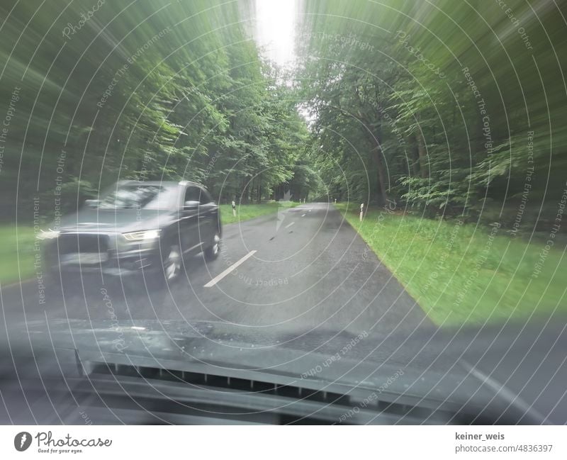 Mit dem Auto durch den grünen Wald auf einer Landstraße fahren bei Regenwetter und Gegenverkehr durch andere PKW KFZ SUV Mittelstreifen Straße Verkehr