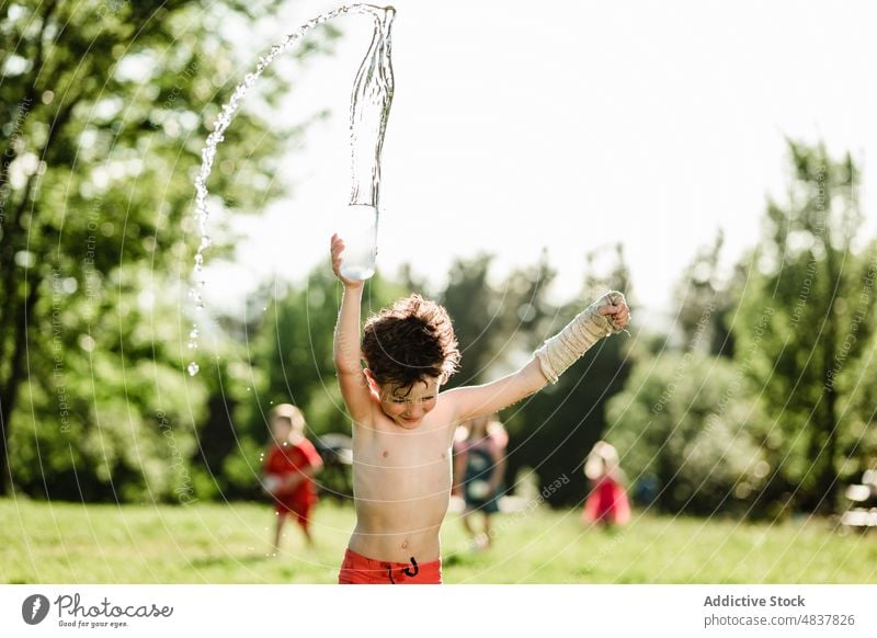 Fröhlicher Junge, der Wasser spritzt Sommer ohne Hemd platschen heiter Glück Eimer Kindheit positiv Rasen Garten Freude Lächeln Feiertag Natur sorgenfrei