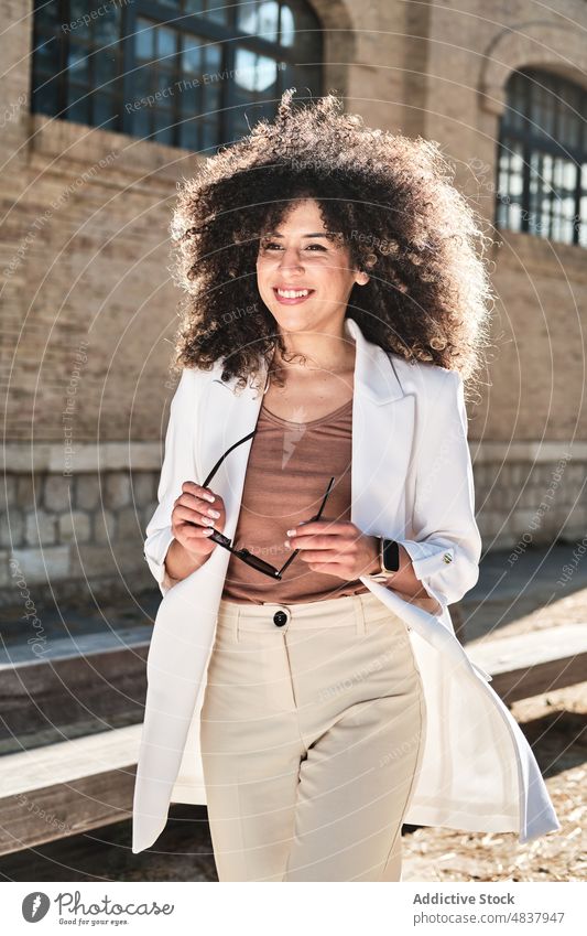 Hispanische Geschäftsfrau mit Sonnenbrille auf der Straße Spaziergang urban Stil selbstbewusst Unternehmer Anzug Frau hispanisch ethnisch schäbig Gebäude trendy