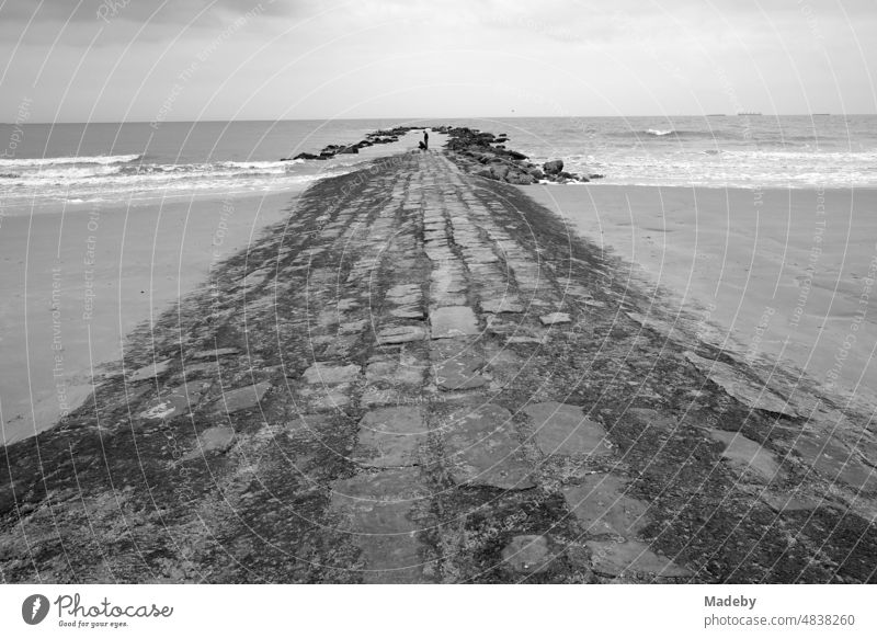 Steine und Mauerwerk als Damm und Wellenbrecher für den Küstenschutz bei Regenwetter am Strand in Knokke-Heist an der Nordsee bei Brügge in Westflandern in Belgien, fotografiert in neorealistischem Schwarzweiß