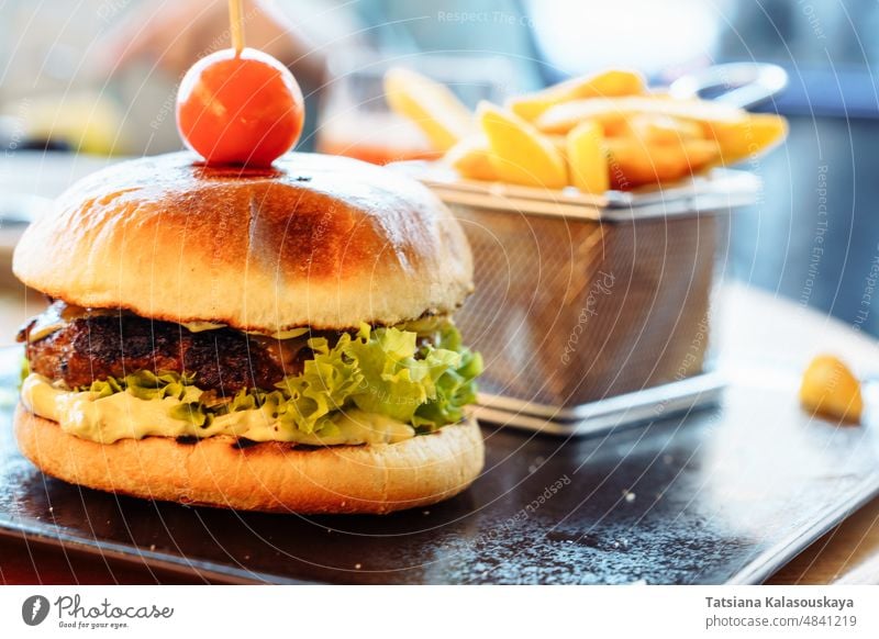 Selektiver Fokus auf einen frischen Burger mit Patty, Kirschtomaten und Salat. Pommes frites im Hintergrund Hamburger Snack Belegtes Brot Fleisch gegrillt