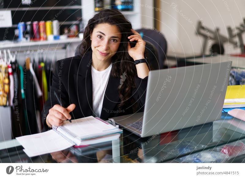 Glücklicher Sportpsychologe schaut in die Kamera Frau Psychologin schreiben Notebook Fitnessstudio Lächeln Psychologie Sitzung Porträt Arbeit Haare berühren