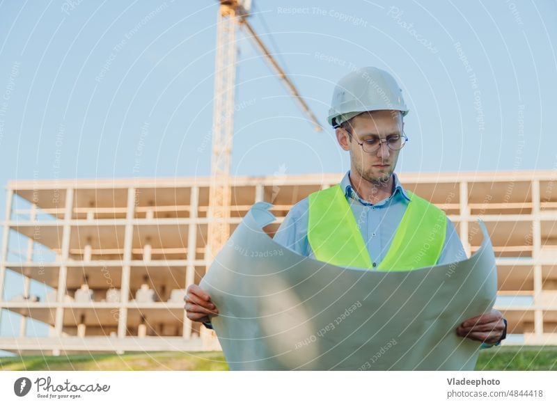 Männlicher Bauingenieur in Helm und Weste bei der Überprüfung einer Bauzeichnung auf der Baustelle Standort Mann Bauplan Projekt Polier Konstruktion